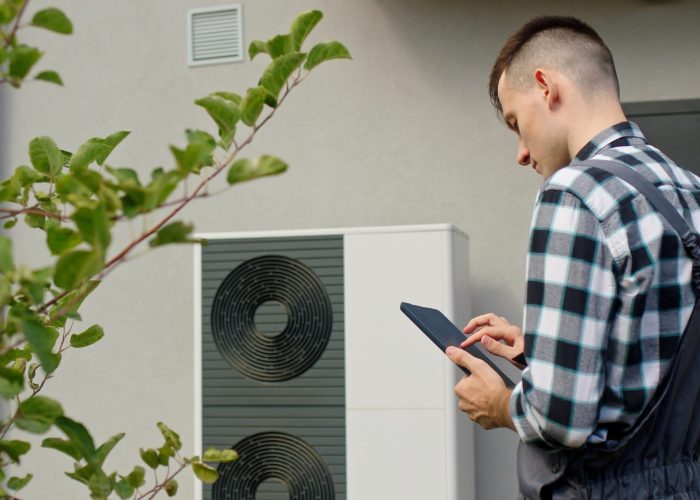 technician-uses-tablet-adjust-settings-external-heat-pump-unit-outside-home-min